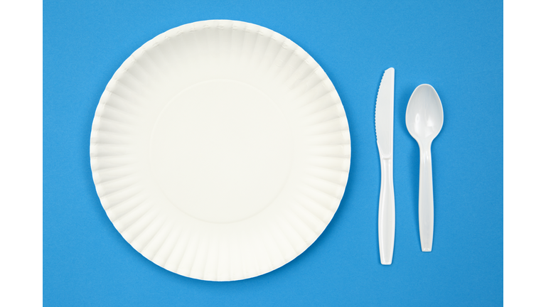 A paper plate next to plastic utensils on a blue table