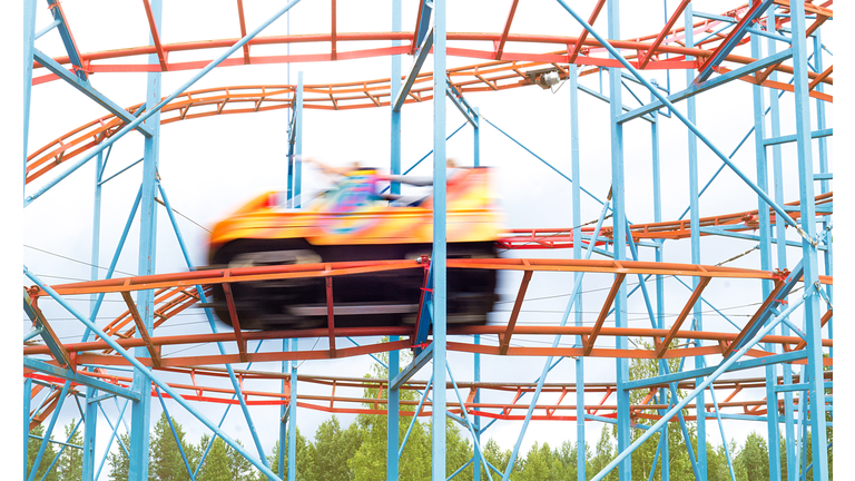 Colorful amusement park ride car going fast by with full speed. People having fun in theme park. Motion blur.