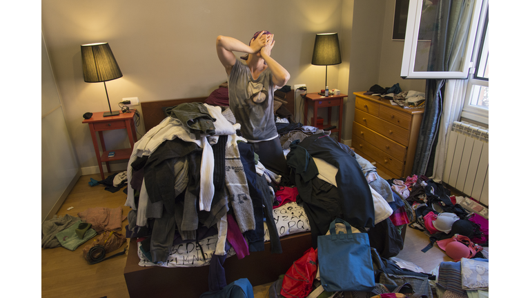 Portrait of woman crying among tiles of clothes in a messy bedroom