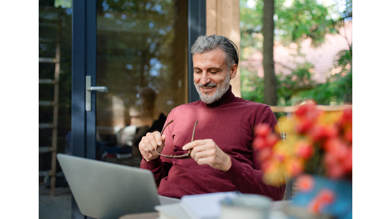 A mature man outdoors by a tree house, using laptop.