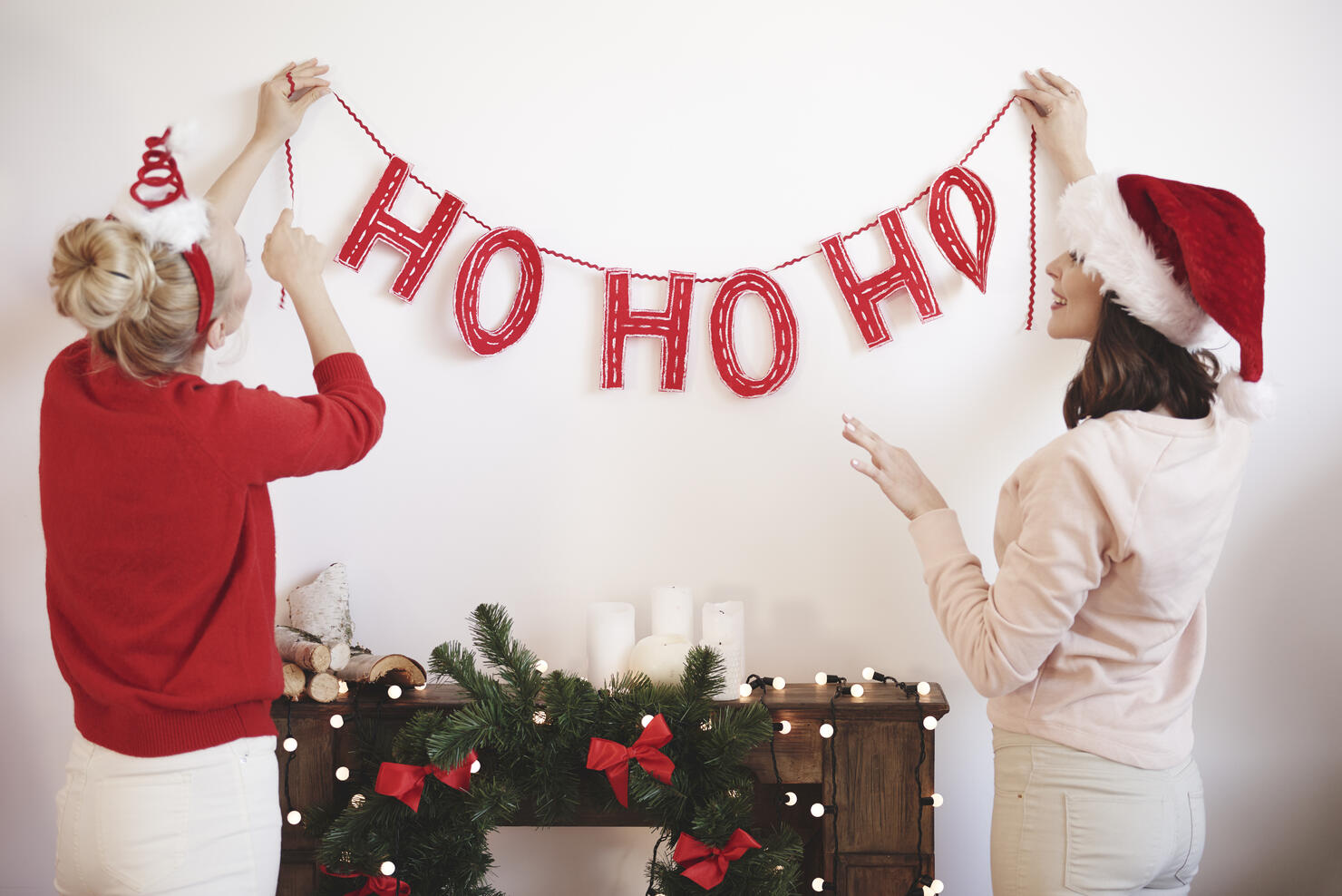 Rear view of two young women putting up christmas decorations on wall