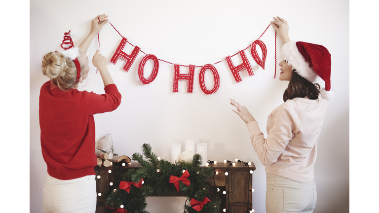 Rear view of two young women putting up christmas decorations on wall