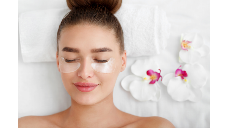 Woman with patches under eyes, relaxing in spa center