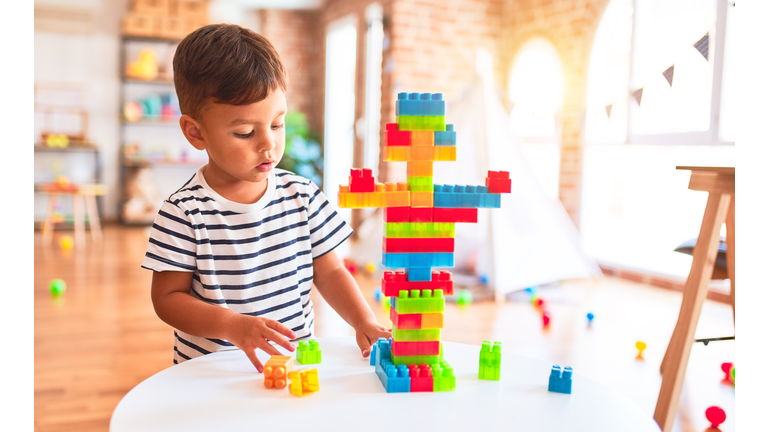 Beautiful toddler boy playing with construction blocks at kindergarten