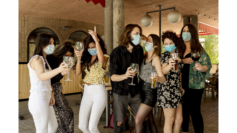 Young friends dancing while holding drinks at restaurant during coronavirus