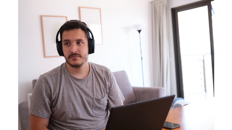 Young man wearing headphones distracted watching series, videos, instead his online classes