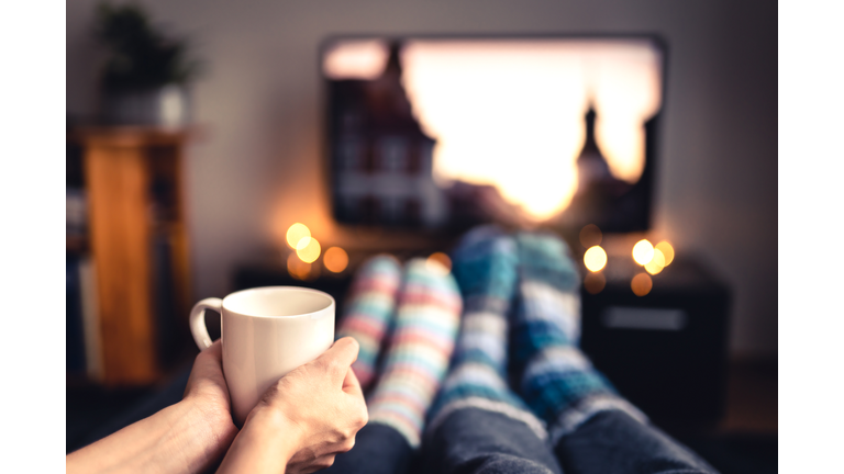 Couple drinking tea, hot chocolate, eggnog or mulled wine and watching tv in warm cozy woolen socks in winter. Woman holding cup of morning coffee in home living room. Sick people with flu.