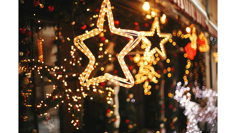 Stylish christmas golden star illumination and fir branches with red and gold baubles, golden lights bokeh on front of building at holiday market in city street. Christmas street decor