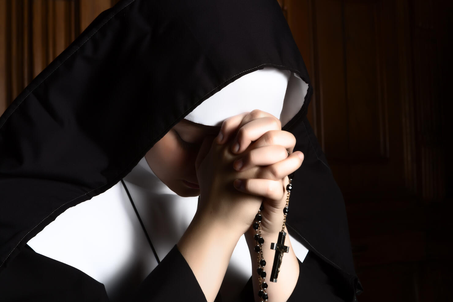 Nun folding hands holding a rosary praying