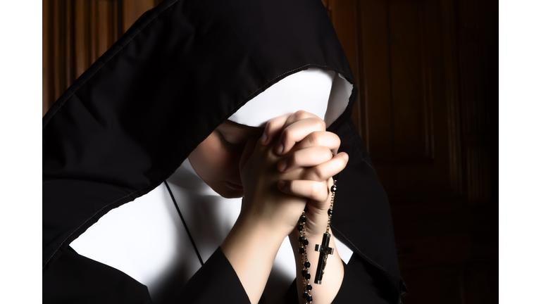 Nun folding hands holding a rosary praying