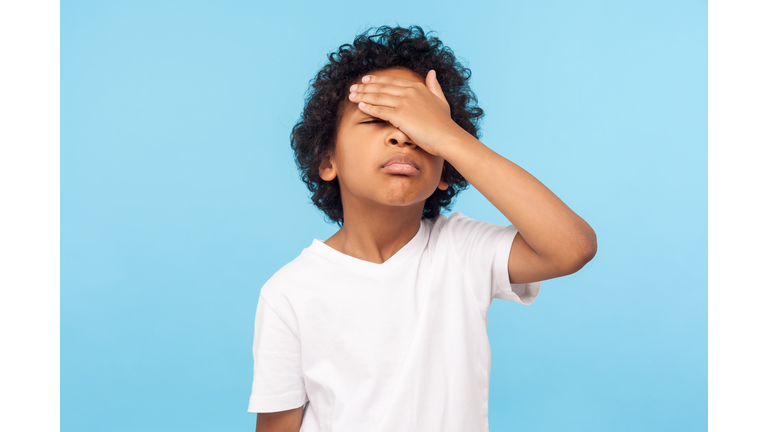 Facepalm. Portrait of forgetful upset little boy with curls covering face with hand and expressing sorrow