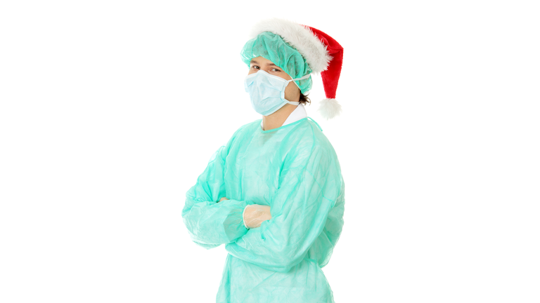 Portrait Of Man Wearing Surgical Mask And Santa Hat Standing Against White Background