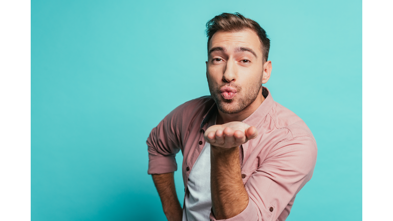 smiling handsome man blowing air kiss isolated on blue