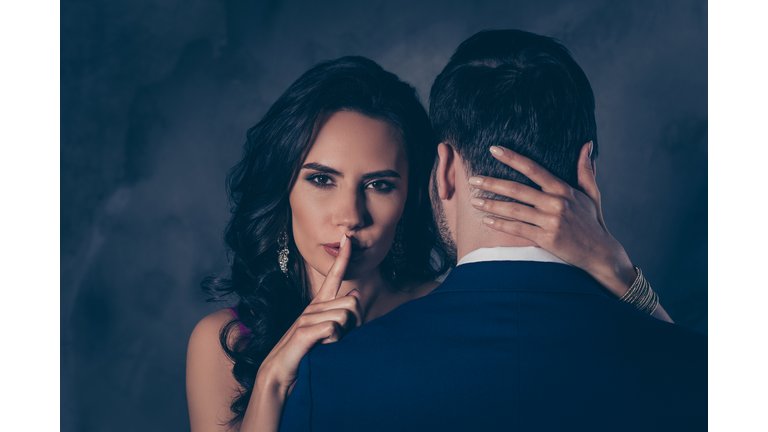 Shh! Portrait of tempting brunette lady showing silence sign with forefinger touching secret mysterious gentlemen with rear view, lovely Mr and Mrs isolated on grey background