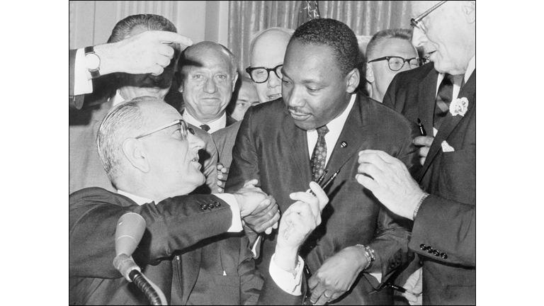 US President Lyndon Johnson (l) shakes hands with the US clergyman and civil rights leader Martin Luther KIng (c) 03 July 1964 in Washington DC, after handing him a pen during the ceremonies for the signing of the civil rights bill at the White House. Martin Luther King was assassinated on 04 April 1968 in Memphis, Tennessee. James Earl Ray confessed to shooting King and was sentenced to 99 years in prison. King's killing sent shock waves through American society at the time, and is still regarded as a landmark event in recent US history. (Photo by - / AFP FILES / AFP) (Photo credit should read -/AFP via Getty Images)