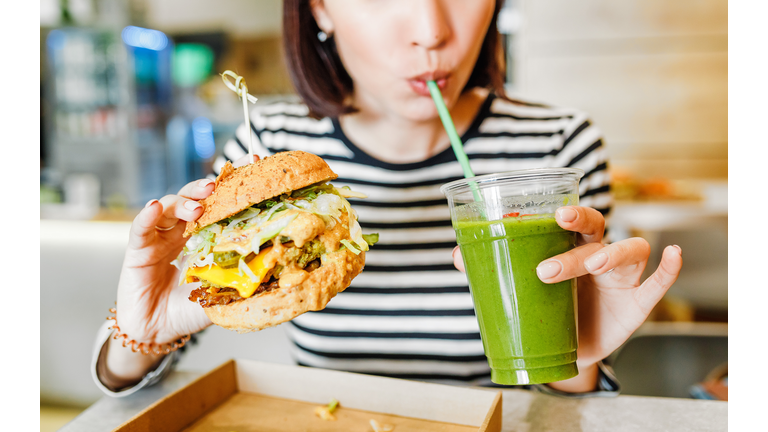 A young woman drinks green smoothies and eats a burger in a vegan fast food restaurant