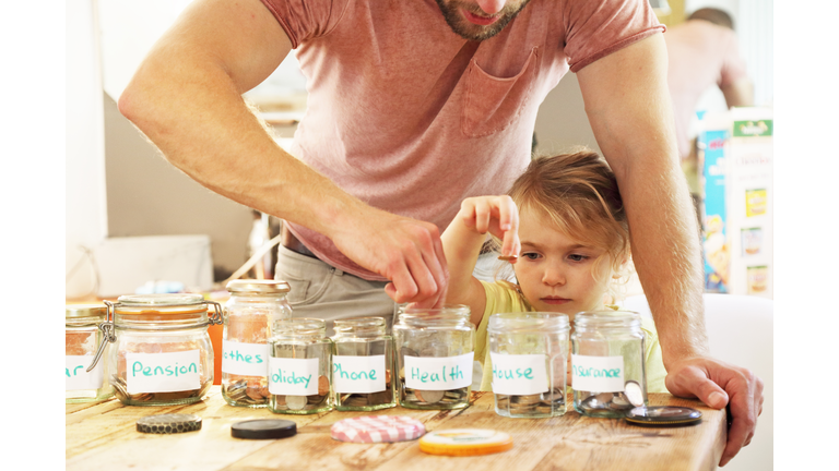 Young girl and father putting money into savings jars