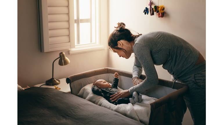 Young mother looking at her baby sleeping in a crib