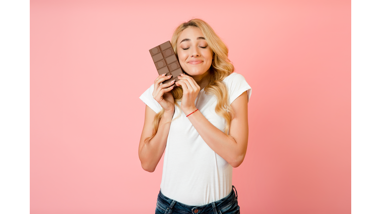 Pretty millennial woman hugging chocolate bar, pink background