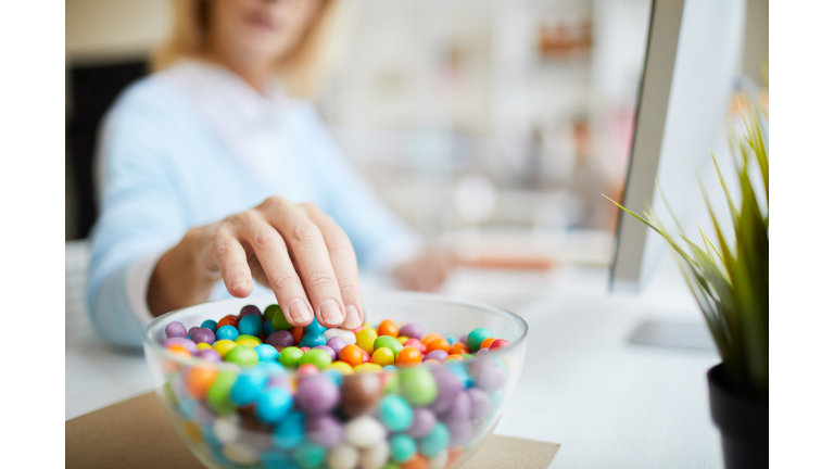 Close-up of unrecognizable businesswoman sitting at table and eating sweet beans while working in office
