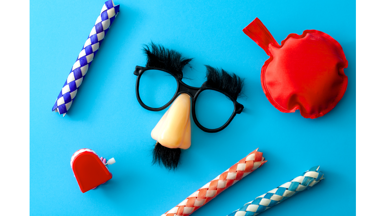 Comical prank, April fools practical joke and goofy disguise concept farting bag, chattering teeth, chinese finger trap and novelty glasses with fake nose and eyebrows isolated on blue background