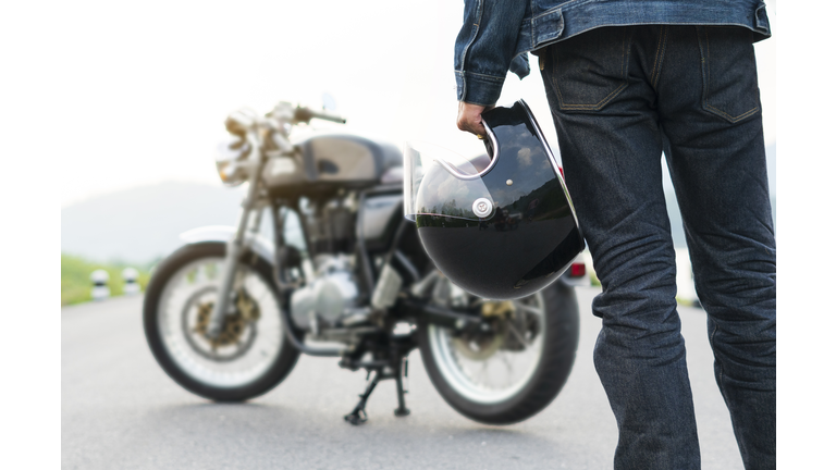 Biker riding in jean is holding a helmet and  motorcycle blur background.