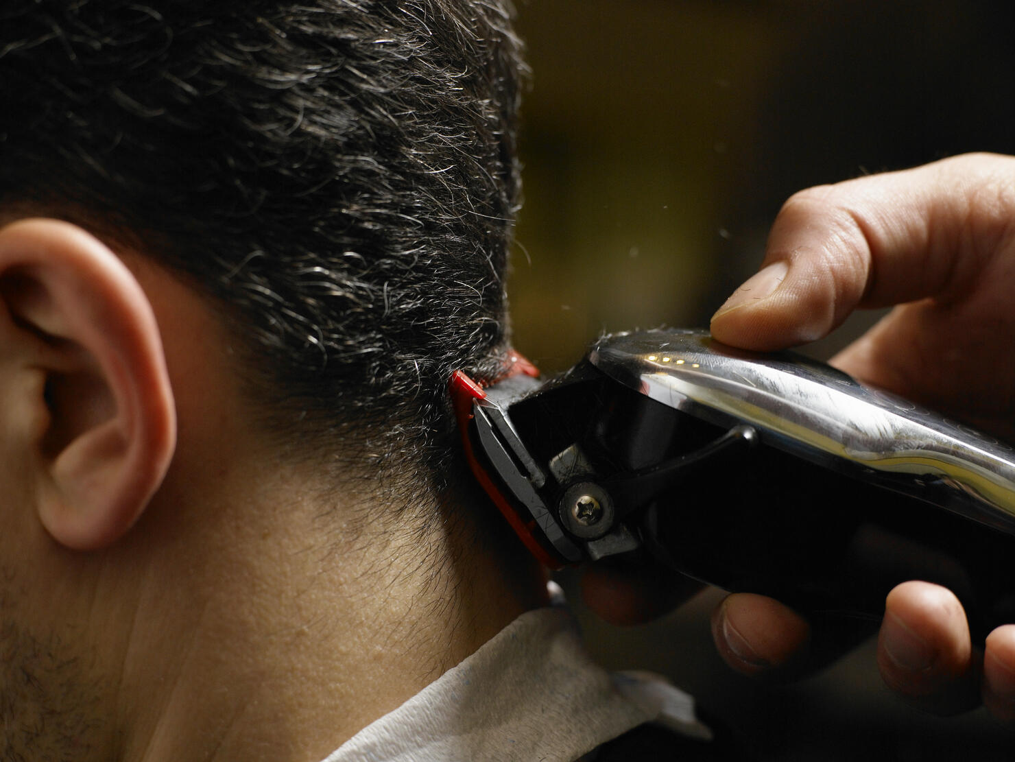 Barber cutting man's hair, close-up of electric razor, side view