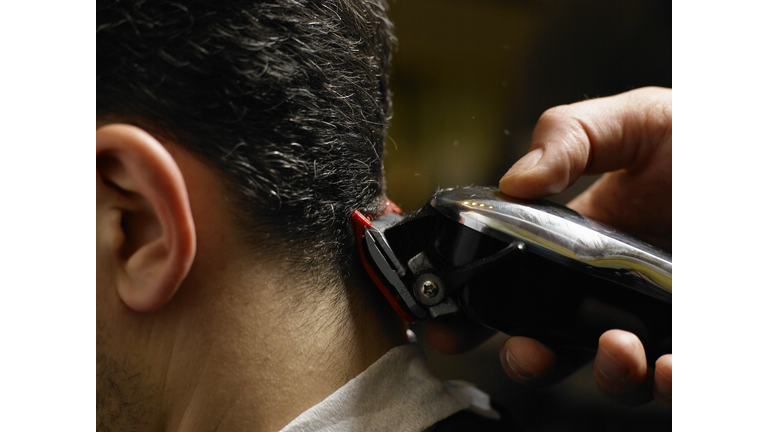 Barber cutting man's hair, close-up of electric razor, side view