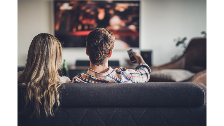 Rear view of a couple watching TV while relaxing on the sofa at home.