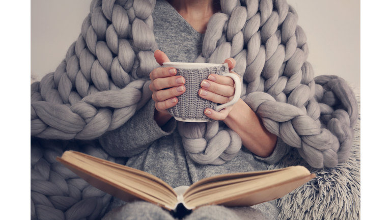 Cozy Woman covered with warm soft merino wool blanket reading a book. Relax, comfort lifestyle.