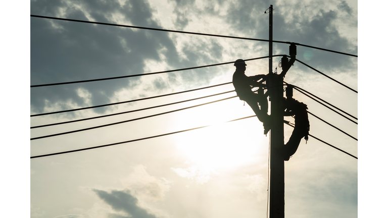 Electrician worker climbing electric power pole to repair the damaged power cable line problems after the storm. Power line support,Technology maintenance and development industry concept