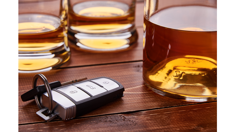 Still life on old wooden table top. Car keys, several glasses and a bottle of whiskey or alcohol. Suitable for drunk driving.