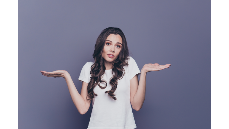 Portrait of magnificent lovely adorable gorgeous stylish nice confused curly-haired girl in casual white t-shirt, showing uncertain gesture, isolated over grey background