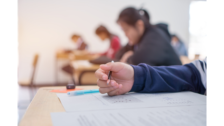 Exams test student in high school, university student holding pencil for testing exam writing answer sheet and exercise for taking in assessment paper on wood table classroom. Education study Concept