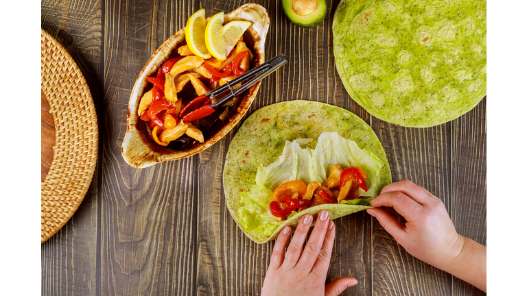 Woman wraping fried chicken with vegetable in pita bread.