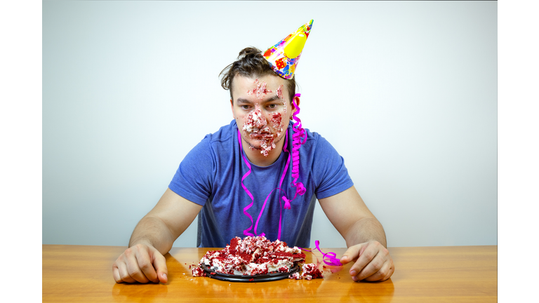 Displeased unhappy caucasian man with cone hat on head and crumple cake  looking down with bored dissatisfied expression as his birthday party sucks. People and lifestyle