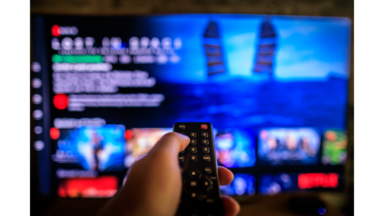 TV remote control in the foreground, Video on demand screen in the blurry background