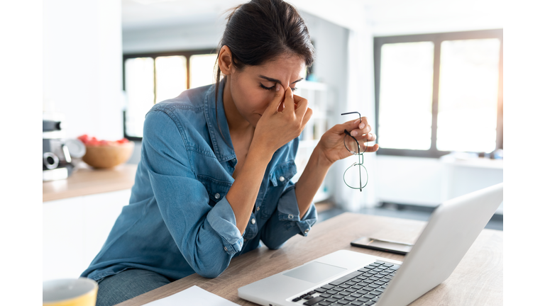 Stressed business woman working from home on laptop looking worried, tired and overwhelmed.