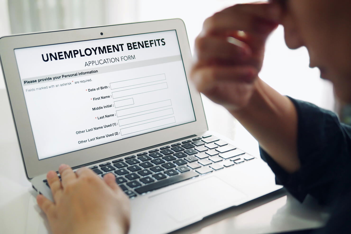 Unemployed depressed person filling out an online unemployment benefits application form using laptop computer.