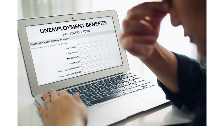 Unemployed depressed person filling out an online unemployment benefits application form using laptop computer.