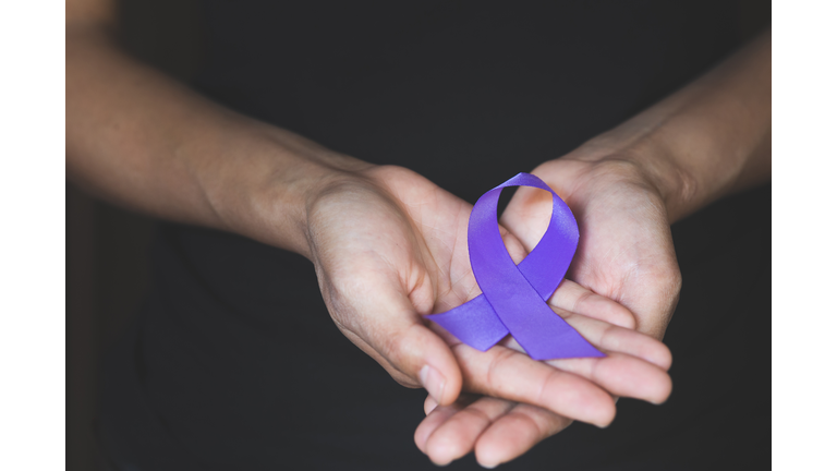 Woman Hand Holding Purple Ribbon, Domestic Violence Awareness Month (October) concept with deep purple awareness ribbon.