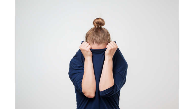 European woman hiding face under the clothes. She is oulling sweater on her head.