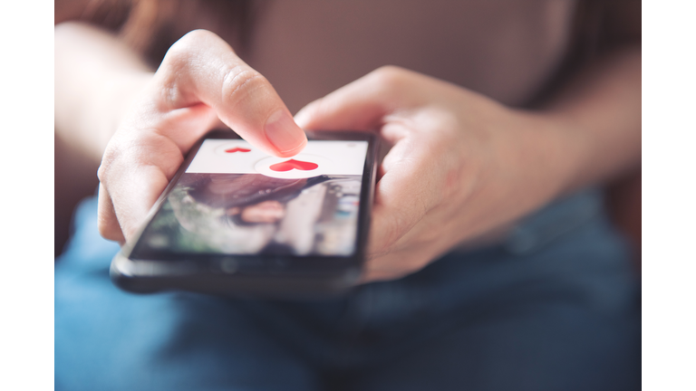 Finger of woman pushing heart icon on screen in mobile smartphone application. Online dating app, valentine's day concept.