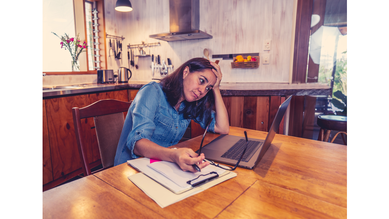 Stressed business woman working from home on laptop looking worried, tired and overwhelmed. Exhausted female working remotely during social distancing. Mental health and coronavirus lockdown.