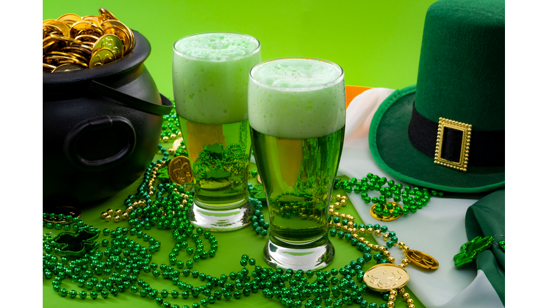 The luck of the Irish meme and Happy St Patricks day concept theme with two glasses of dyed beer, leprechaun hat, beads necklace and pot of gold coins on the Ireland flag isolated on green background