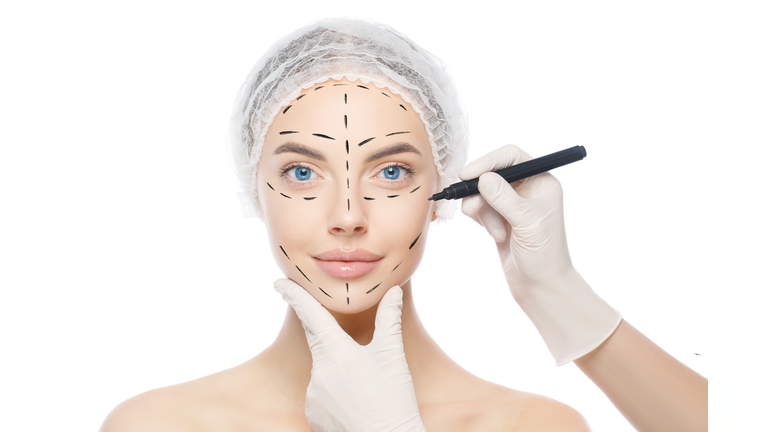 Plastic surgery or face lifting for young woman. Doctor's hands wearing gloves drawing lines, holding head of female patient, isolated on white background