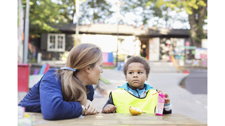 Angry teacher looking at student holding juice box outside kindergarten