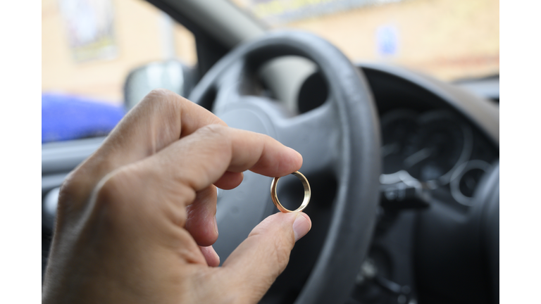 Man´s hand holding a gold wedding ring inside a parked car.