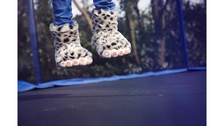 Child wearing novelty monster feet slippers, jumping on a trampoline