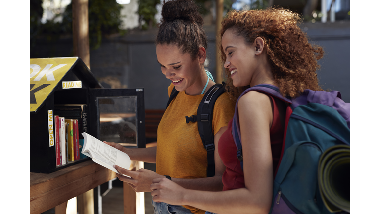 Young women with backpacks smiling, while choosing books